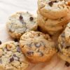 Stack of walnut chocolate chip cookies with visible chunks of walnuts and chocolate chips, on a wooden board with scattered chocolate chips around.