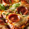 Close-up of a Cauliflower Crust Pepperoni Pizza with melted cheese strings, pepperoni, and a garnish of fresh basil, highlighting the textured cauliflower crust.