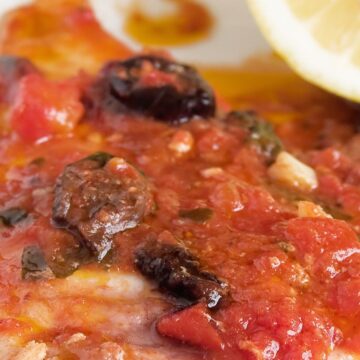 Close-up view of Quick and Easy Italian Fish Fillets topped with a savory sauce of tomatoes, olives, and herbs, ready to be served.