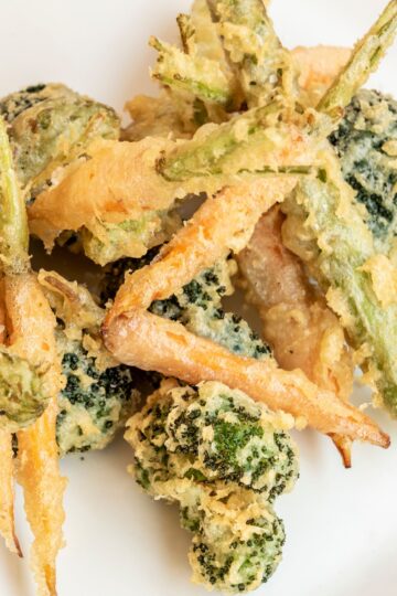 Close-up of oven-baked vegetable tempura, showcasing crispy carrot sticks, broccoli florets, and green beans covered in a crunchy coating.