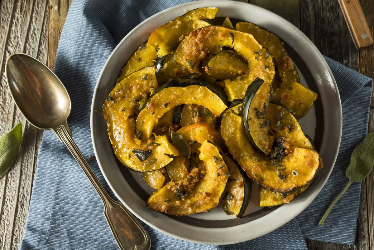 Top view of a plate of roasted acorn squash wedges with a miso honey glaze, garnished with herbs, accompanied by a vintage spoon on a wooden table with a blue napkin.