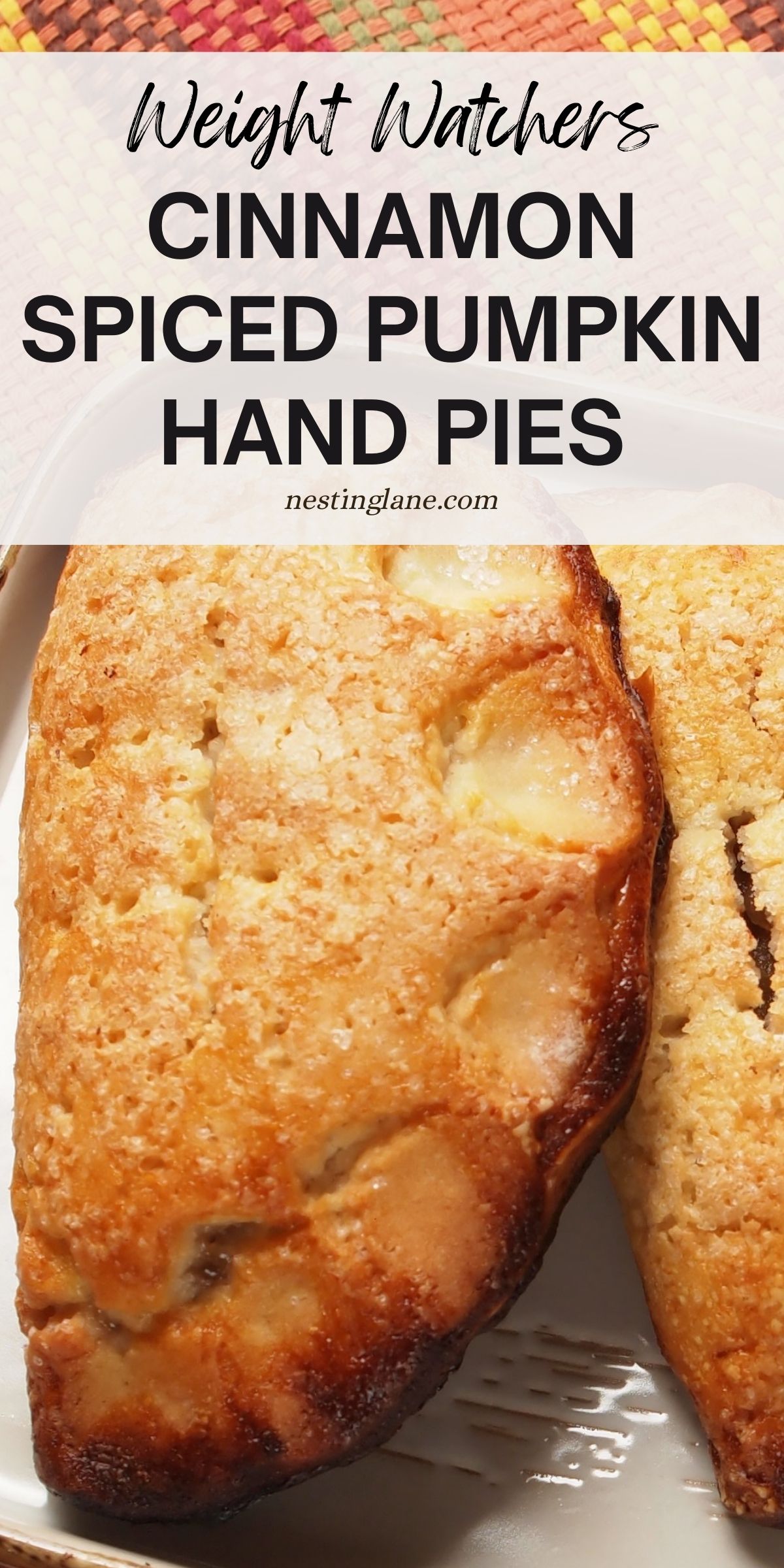 Golden cinnamon spiced pumpkin hand pie with a sugared crust, baked until flaky and crisp. The pastry rests on a white dish with a colorful woven fall placemat in the background. Text overlay reads “Weight Watchers Cinnamon Spiced Pumpkin Hand Pies” with nestinglane.com beneath.