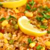 Close-up of a taco beef skillet dinner with rice, corn, peas, diced vegetables, and fresh parsley. Lemon wedges sit on top, adding a bright garnish to the colorful, hearty dish served in a cast iron pan.