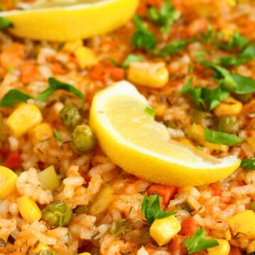 Close-up of a taco beef skillet dinner with rice, corn, peas, diced vegetables, and fresh parsley. Lemon wedges sit on top, adding a bright garnish to the colorful, hearty dish served in a cast iron pan.