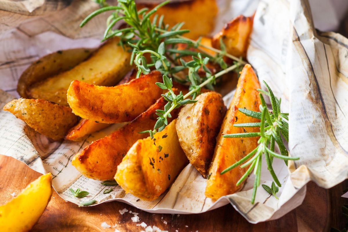 Golden roasted potato wedges served on rustic parchment, garnished with fresh rosemary and thyme. The crispy edges and fluffy centers make these herb-seasoned potatoes a perfect side dish for healthy dinner ideas.