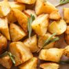 Closeup Crispy roasted potato chunks with golden-brown edges, seasoned with herbs and garnished with fresh rosemary sprigs, served on parchment paper for a rustic presentation.