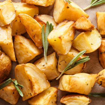 Closeup Crispy roasted potato chunks with golden-brown edges, seasoned with herbs and garnished with fresh rosemary sprigs, served on parchment paper for a rustic presentation.
