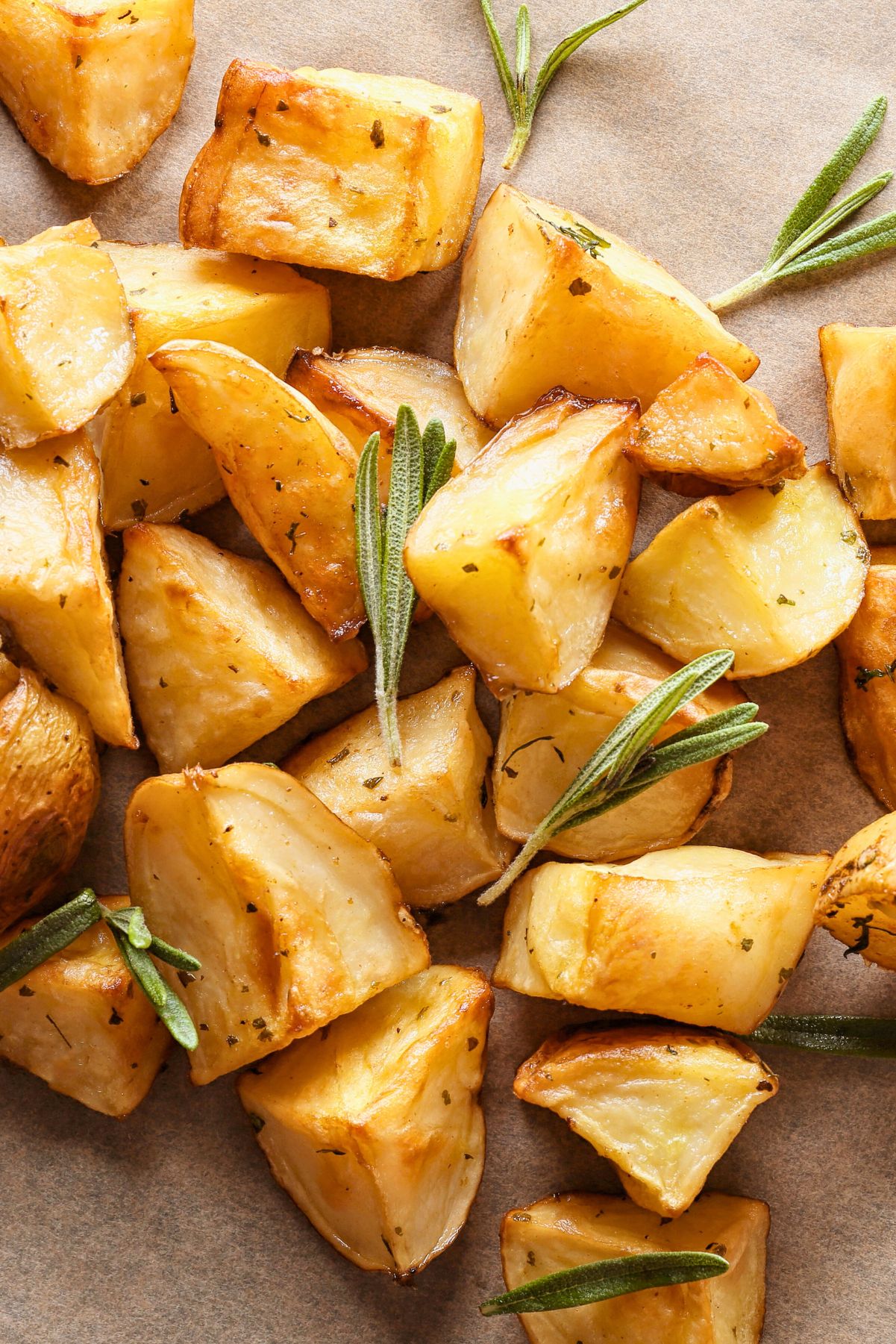 Closeup Crispy Roasted Rosemary Potatoes with golden-brown edges, seasoned with herbs and garnished with fresh rosemary sprigs, served on parchment paper for a rustic presentation.