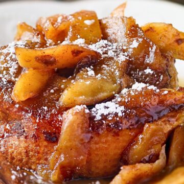 Close-up of slow cooker apple cinnamon French toast casserole topped with caramelized apple slices, warm cinnamon glaze, and a dusting of powdered sugar. The golden bread soaks up the spiced sauce, creating a rich and cozy fall breakfast or brunch dish.