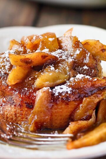Close-up of slow cooker apple cinnamon French toast casserole topped with caramelized apple slices, warm cinnamon glaze, and a dusting of powdered sugar. The golden bread soaks up the spiced sauce, creating a rich and cozy fall breakfast or brunch dish.