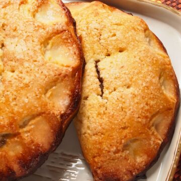 Golden brown pumpkin hand pies with a sugared crust, baked until crisp and flaky. The pastries are filled with spiced maple pumpkin and displayed on a white dish over a colorful woven placemat.