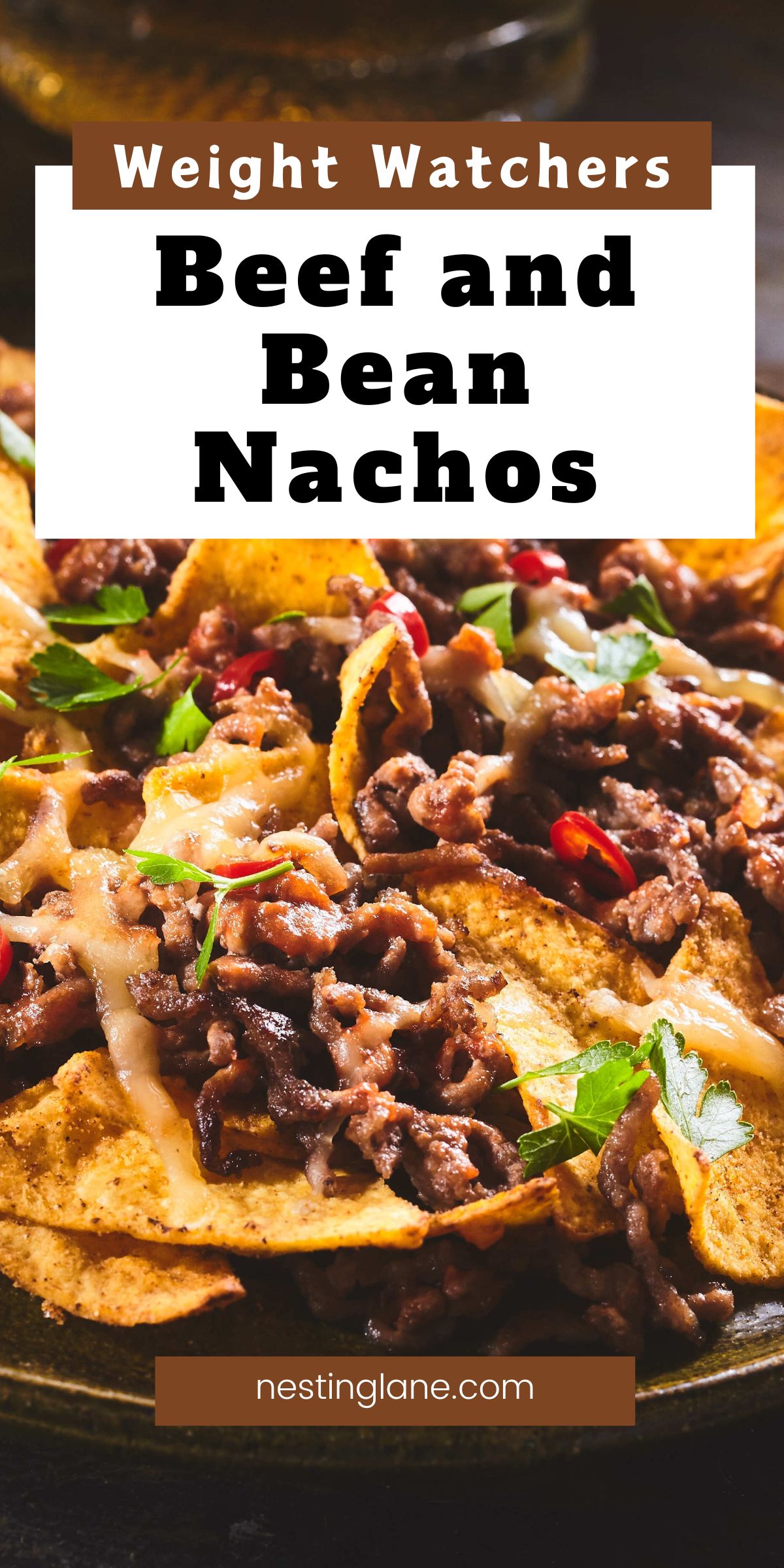 Close-up of beef and bean nachos: crunchy tortilla chips piled with seasoned ground beef, melted cheese, parsley, and sliced red chiles on a dark plate. Text reads “Weight Watchers Beef and Bean Nachos” and “nestinglane.com.” Keywords: beef and bean nachos, easy recipe, game day appetizer, weeknight dinner.