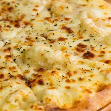 Close-up of a sliced pita pizza with bubbly melted mozzarella and a sprinkle of dried herbs on a wooden board, golden crust and a soft, chewy center in view; easy 10-minute pita pizza, garlic cheese flatbread, quick weeknight dinner.