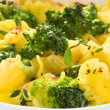 Close-up of baked broccoli macaroni and cheese in a white casserole dish: ruffled pasta coated in gooey cheddar, roasted broccoli florets, fresh thyme, black pepper, and red pepper flakes. Comfort food dinner, vegetarian pasta bake.