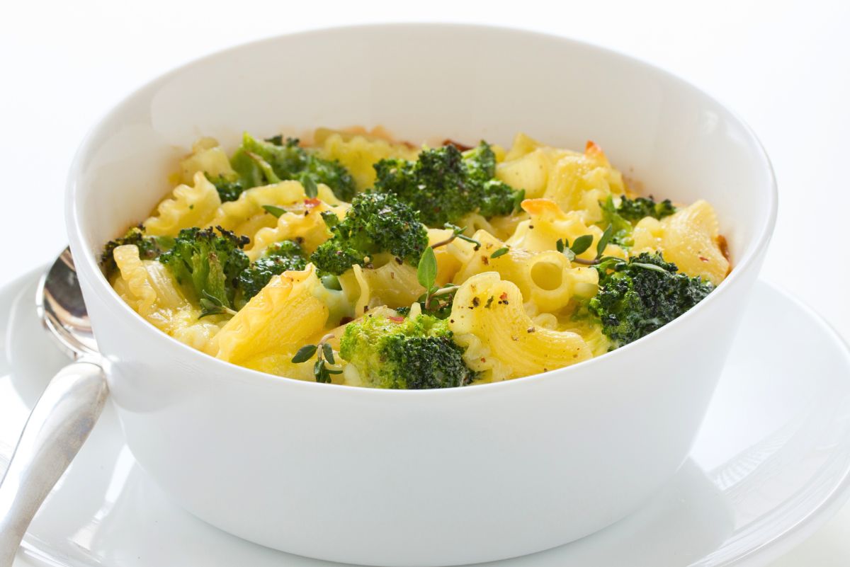 White bowl of baked broccoli macaroni and cheese; ruffled pasta coated in creamy cheddar with roasted broccoli florets, fresh thyme, black pepper, and red pepper flakes. Comfort food casserole, vegetarian pasta bake, easy weeknight dinner recipe.