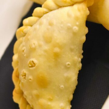 Close-up of a golden baked pear ginger hand pie with a lightly blistered crust and braided crimped edge, resting on a black napkin over a white plate. Dessert pastry turnover; baked pear ginger hand pie recipe.