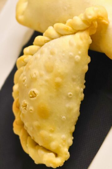 Close-up of a golden baked pear ginger hand pie with a lightly blistered crust and braided crimped edge, resting on a black napkin over a white plate. Dessert pastry turnover; baked pear ginger hand pie recipe.