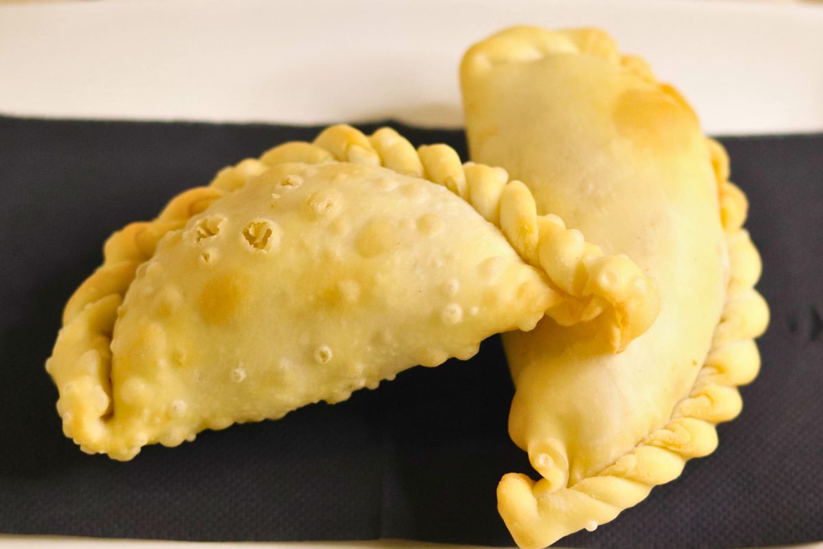 Two golden baked pear ginger hand pies with crimped braided edges and a lightly blistered crust, stacked on a black napkin over a white plate. Handheld dessert pastry turnovers; baked pear ginger hand pies recipe.