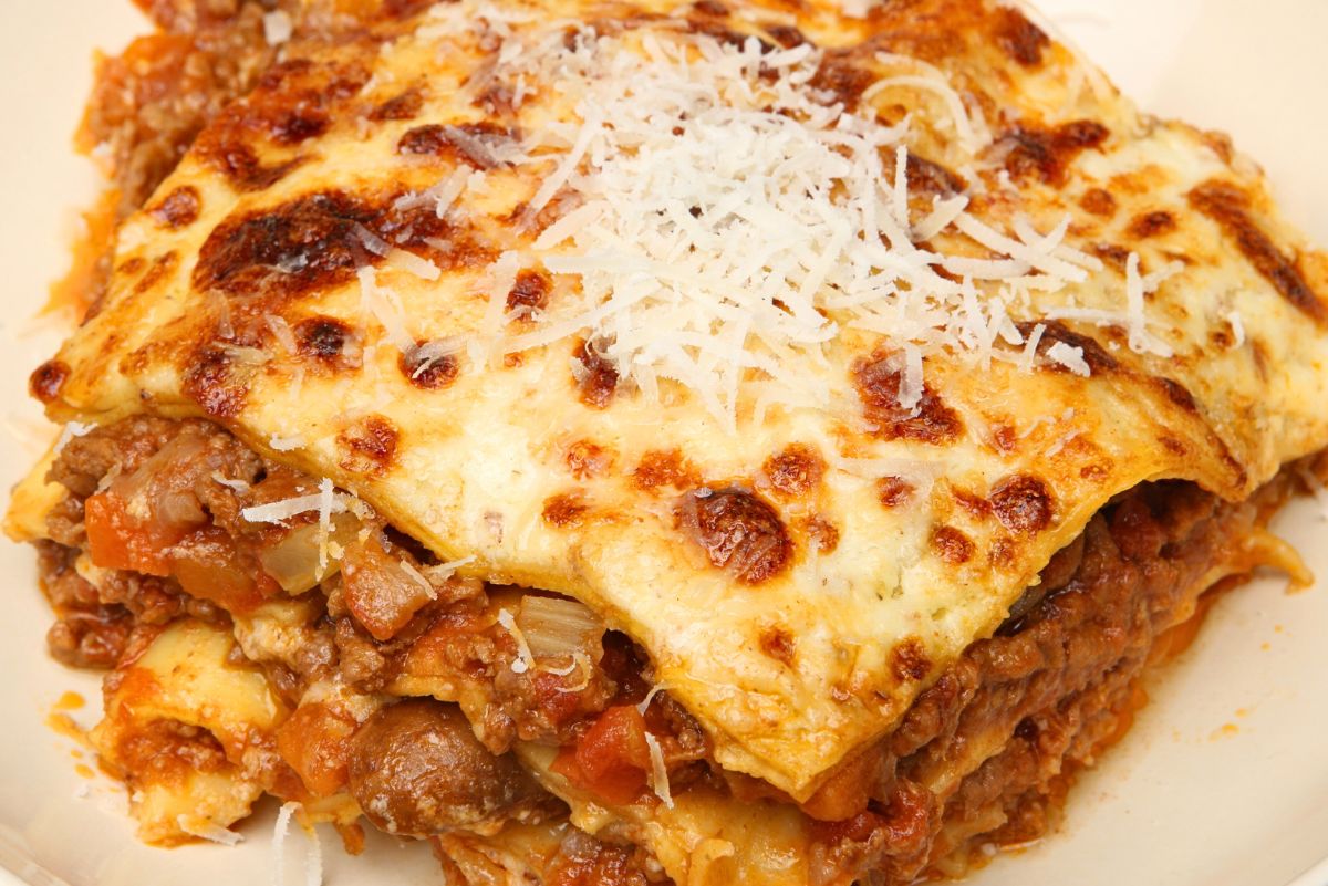 Close-up slice of crockpot lazy lasagna with golden, bubbly cheese and a sprinkle of shredded Parmesan over layered noodles, beef, and tomato sauce. Hearty slow cooker pasta, easy dinner recipe, comfort food.