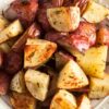 Close-up of roasted red potatoes with rosemary, quartered and golden with crispy edges in a white bowl on a rustic wood table. Coarse salt and herbs visible. Keywords: roasted red potatoes, rosemary potatoes, easy side dish, oven roasted recipe.