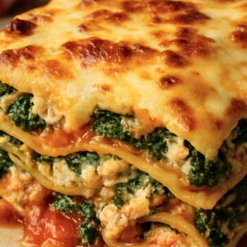 Close-up of ground chicken and spinach lasagna: golden, bubbly mozzarella on top, layered pasta with ricotta and spinach, and tomato sauce oozing onto a beige plate. Italian comfort food, high-protein chicken lasagna dinner recipe.