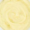 Creamy cauliflower mashed potatoes in a white bowl, smooth swirled texture on a rustic white wood background.