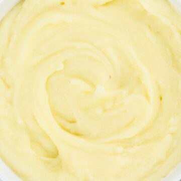 Creamy cauliflower mashed potatoes in a white bowl, smooth swirled texture on a rustic white wood background.