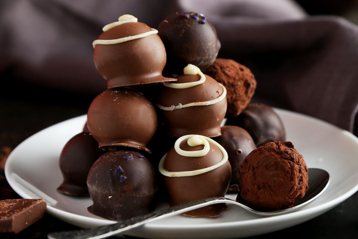 Plate of no-bake chocolate cream cheese truffles stacked in a pyramid—milk and dark chocolate shells with white chocolate swirls, plus cocoa-dusted truffles—served with a spoon on a white plate; rich homemade candy, dessert, holiday treat.