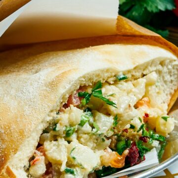 Air fryer cauliflower pita filled with tender roasted cauliflower, fresh herbs, and creamy tahini sauce inside a soft, lightly toasted pita pocket. Close-up shows chunky cauliflower pieces, green herbs, and rich sauce on a plate with fresh ingredients blurred in the background.