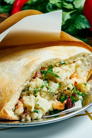 Air fryer cauliflower pita filled with tender roasted cauliflower, fresh herbs, and creamy tahini sauce inside a soft, lightly toasted pita pocket. Close-up shows chunky cauliflower pieces, green herbs, and rich sauce on a plate with fresh ingredients blurred in the background.