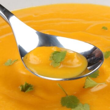 Easy Butternut Squash Soup in a white bowl with a spoon hovering over it.