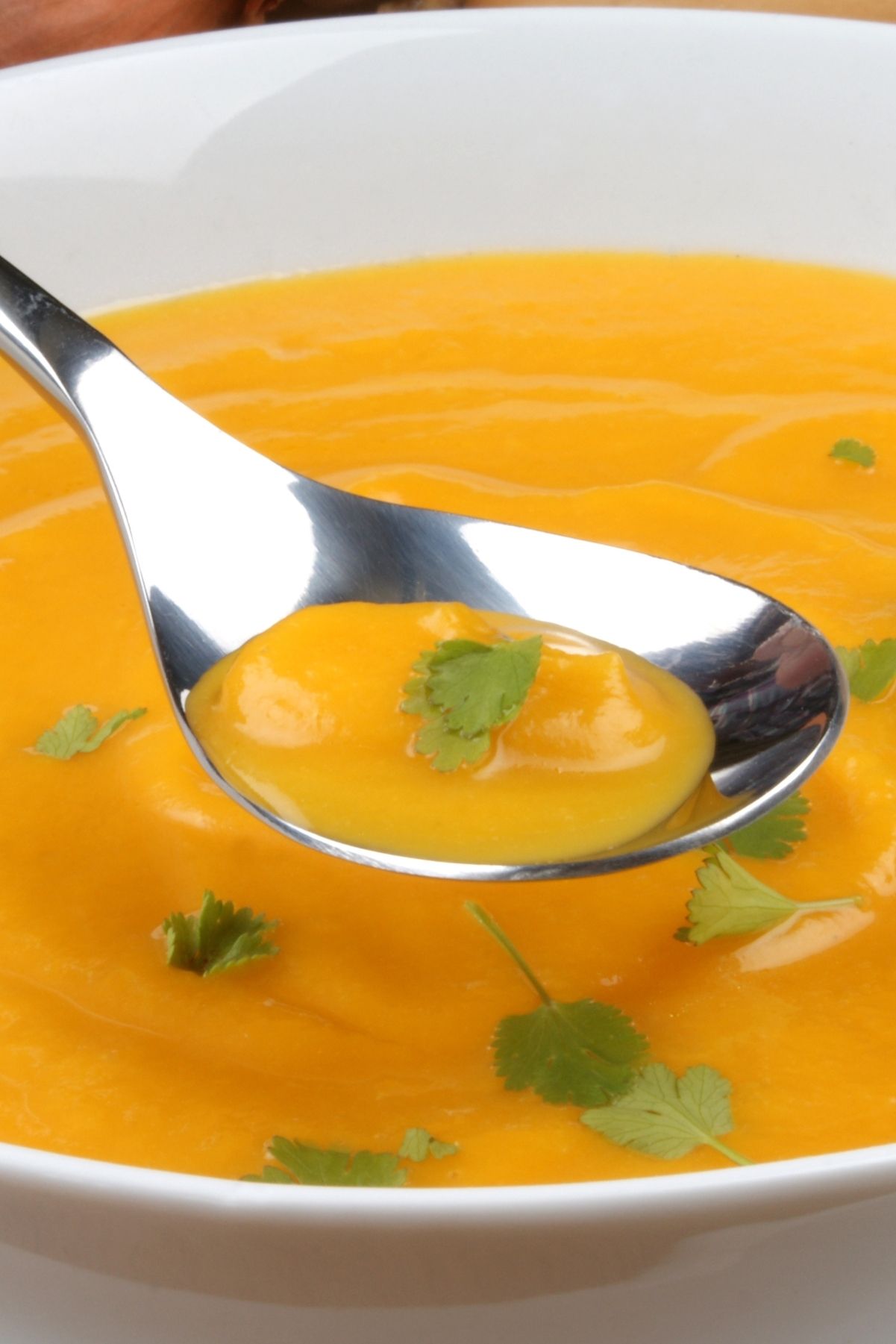 Easy Butternut Squash Soup in a white bowl with a spoon hovering over it.