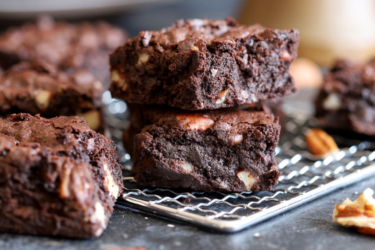 Homemade chocolate walnut brownies stacked on a metal cooling rack, showing thick, fudgy layers with visible walnut pieces throughout. Rich dark chocolate brownies with a dense crumb and slightly crackled tops, photographed close up on a dark kitchen surface.