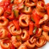 Cheese tortellini tossed in rich tomato sauce with sliced zucchini and tender tomato pieces, served in a white bowl. Close-up view highlights the soft stuffed pasta, glossy red sauce, and green zucchini for a hearty crockpot pasta dinner.