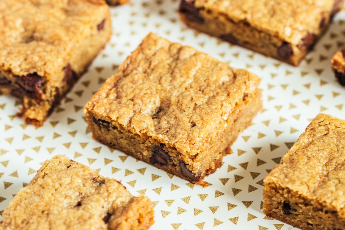 Easy chocolate chip dessert bars cut into squares, showing a golden brown baked top and soft interior with chocolate chips. Bars are spaced on a light plate with a small gold triangle pattern, highlighting a simple WW friendly dessert bar with a chewy homemade texture.