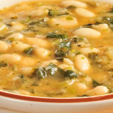 Creamy white bean and kale soup in a ceramic bowl, with tender white beans, chopped kale, and a light golden broth. Hearty vegetable soup with a smooth texture, visible greens, and beans throughout, served warm on a wooden table for a cozy, healthy meal.