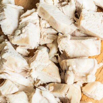 Close-up overhead of chopped, shredded cooked chicken breast on a wooden cutting board, moist white meat ready for salads, soups, or high-protein Instant Pot recipes.