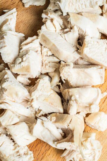 Close-up overhead of chopped, shredded cooked chicken breast on a wooden cutting board, moist white meat ready for salads, soups, or high-protein Instant Pot recipes.