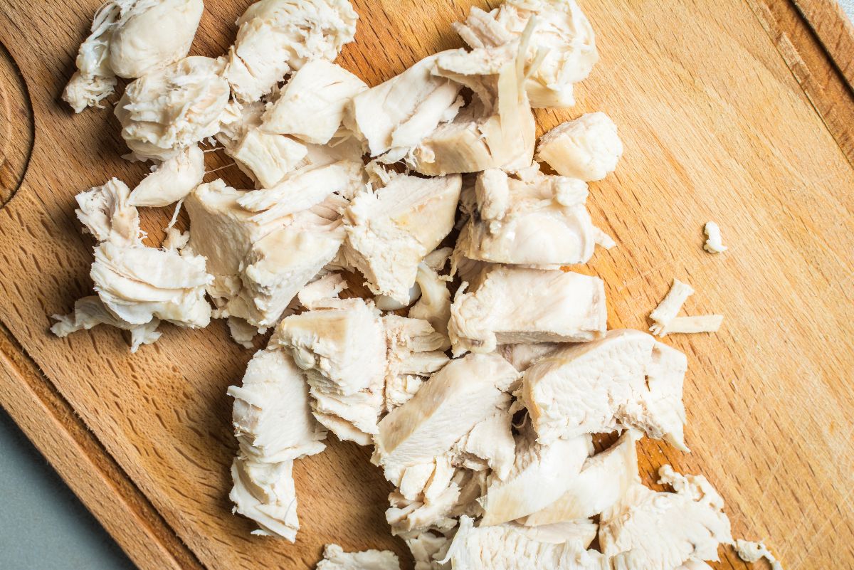 Close-up of chopped, cooked chicken breast on a wooden cutting board.