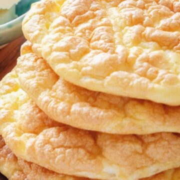 Stack of homemade low carb cloud bread rounds with a fluffy, airy texture and lightly golden tops, resting on a wooden surface. Soft, pillowy bread made with simple ingredients, showing a cloud-like interior and delicate browned edges, styled for healthy Weight Watchers friendly baking.