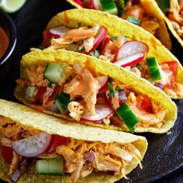 Slow Cooker Mexican Chicken Taco Meat in tacos on a dark surface.