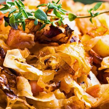 Close-up of a cabbage skillet with bacon and potatoes, showing golden caramelized cabbage, crispy bacon pieces, and tender potato chunks cooked in a pan, topped with fresh green herb sprigs. Rustic skillet dinner with savory cabbage and potatoes.