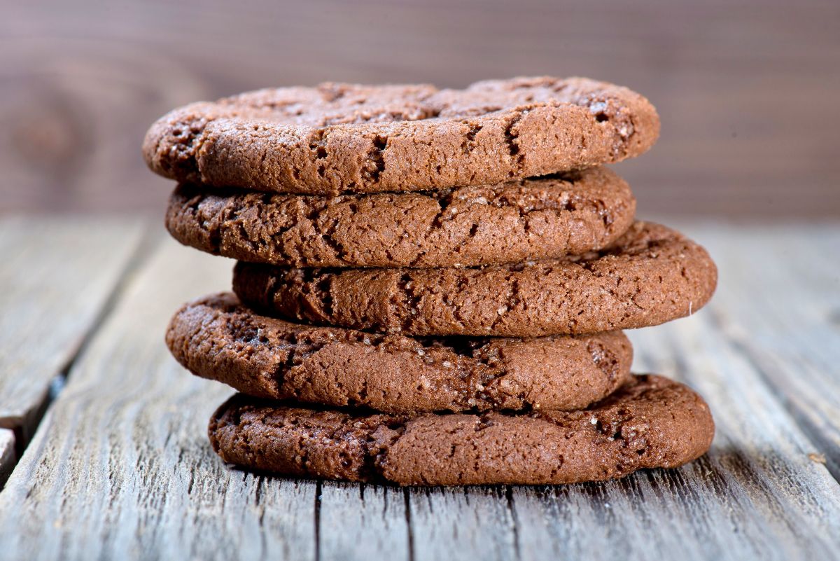 Stack of chocolate cayenne almond cookies with a thick, soft-baked texture and lightly cracked tops. Rich brown cookies are layered neatly on a rustic wooden surface, showing a dense, chewy crumb with subtle sugar crystals and a homemade chocolate almond cookie finish.