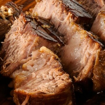 Close-up of sliced crockpot Italian beef roast on a wooden cutting board, showing tender, juicy beef with browned edges and visible cooking juices. High protein slow cooker beef roast with rich texture and savory appearance.