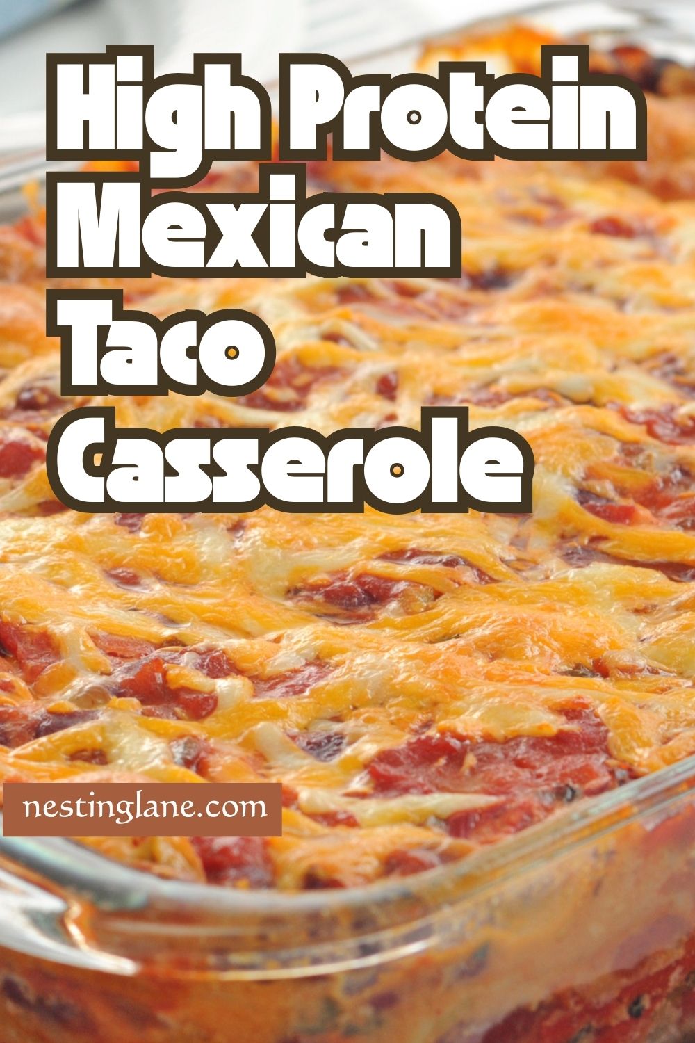 High protein Mexican beef taco casserole baked in a clear glass baking dish, layered with seasoned ground beef, tortillas, tomato sauce, and melted shredded cheese. Close-up shows a cheesy, bubbly top with red and golden tones. Text on image reads “HIGH PROTEIN Mexican Beef Taco Casserole” and “SAVE FOR LATER” with “NESTINGLANE.COM” at the bottom.