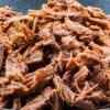 Close-up of high protein orange and cumin pulled pork in a dark bowl, showing tender shredded pork coated in warm orange and cumin spices. Juicy, slow cooked pulled pork with a rich, savory texture against a rustic wooden background.
