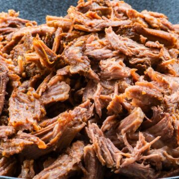 Close-up of high protein orange and cumin pulled pork in a dark bowl, showing tender shredded pork coated in warm orange and cumin spices. Juicy, slow cooked pulled pork with a rich, savory texture against a rustic wooden background.