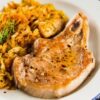 Golden brown skillet pork chop seasoned with black pepper on a white plate, served with sautéed cabbage, carrots, and diced vegetables. Close-up view shows a juicy pork chop with crisp edges and tender cooked veggies, highlighting a high protein one-skillet dinner.