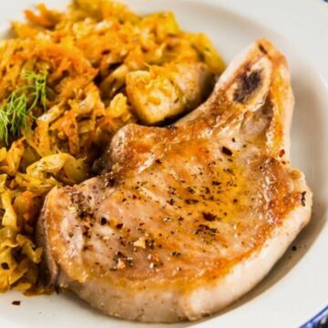 Golden brown skillet pork chop seasoned with black pepper on a white plate, served with sautéed cabbage, carrots, and diced vegetables. Close-up view shows a juicy pork chop with crisp edges and tender cooked veggies, highlighting a high protein one-skillet dinner.