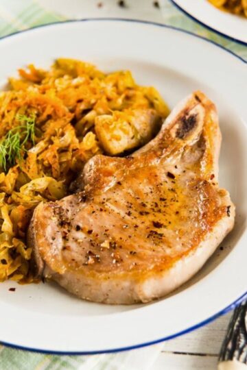 Golden brown skillet pork chop seasoned with black pepper on a white plate, served with sautéed cabbage, carrots, and diced vegetables. Close-up view shows a juicy pork chop with crisp edges and tender cooked veggies, highlighting a high protein one-skillet dinner.